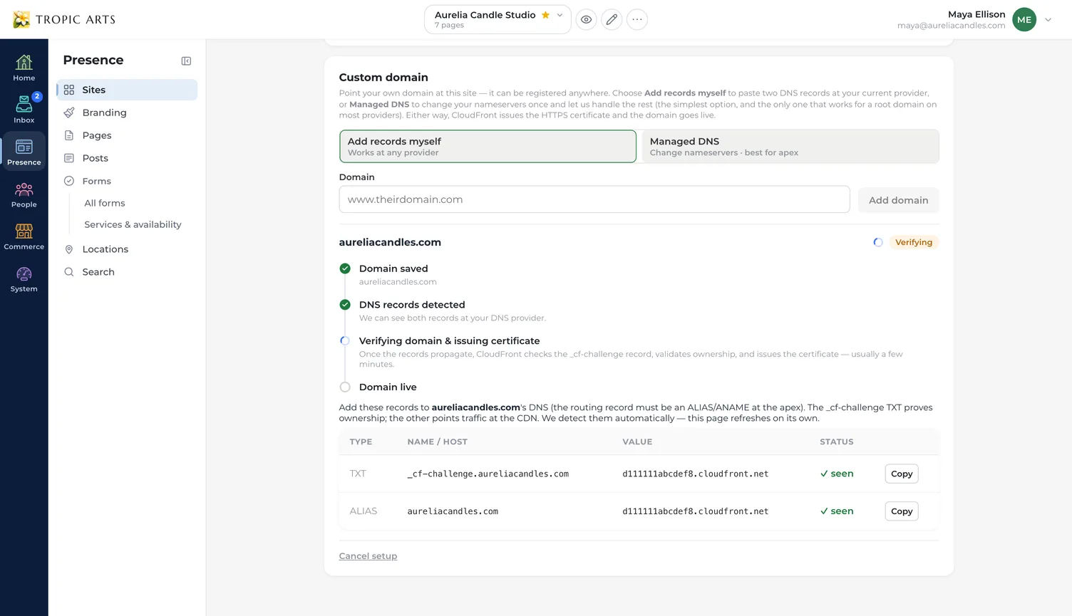 The Custom domain card in a site’s domain settings, offering a choice between adding two DNS records yourself and handing over nameservers, with a box to enter the domain. Below it aureliacandles.com sits mid-setup — saved and its records detected, the certificate still being issued, the domain not yet live — above a table of the TXT and ALIAS records to add, each marked as seen.